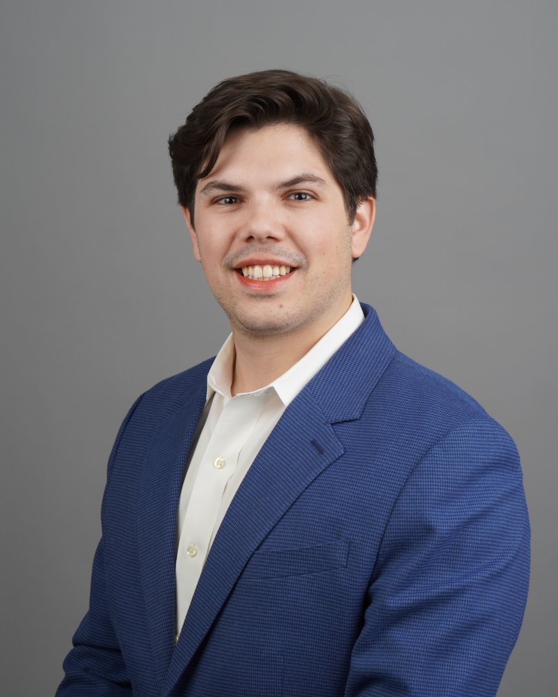 Eric Hirsh, President of E4 Solutions LLC, wearing a blue blazer against a gray backdrop