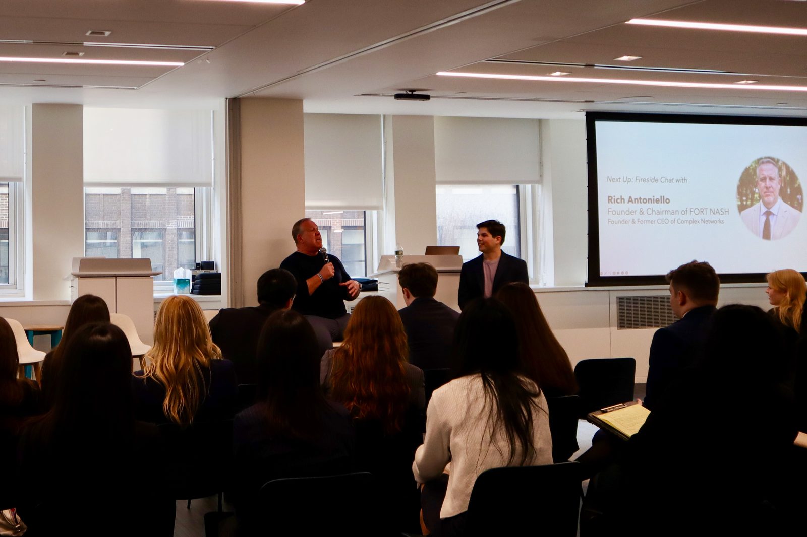Eric Hirsh on stage during a fireside chat with Rich Antoniello, with audience members seated in the foreground